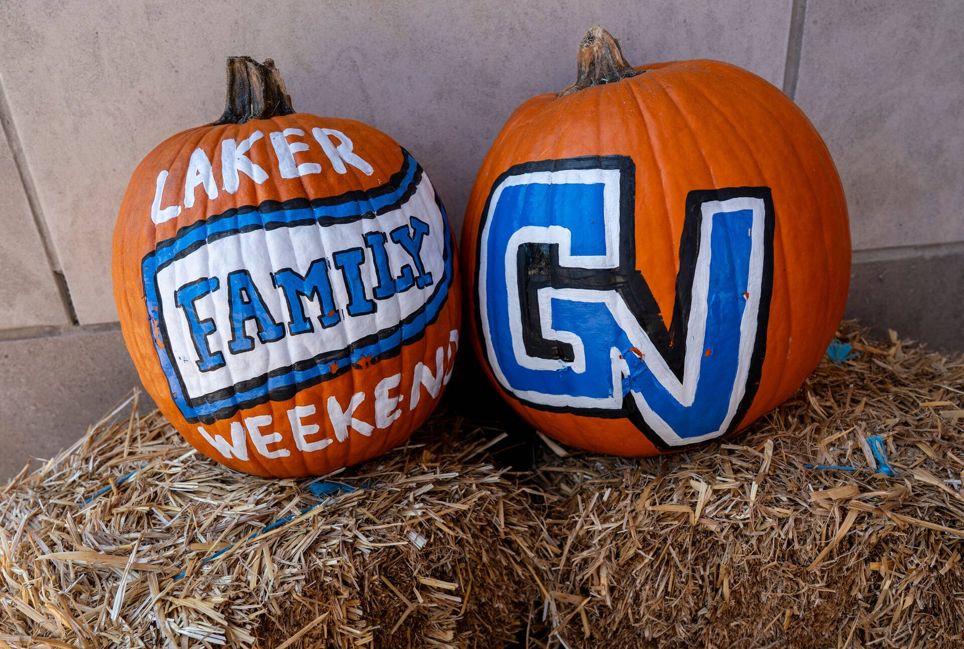 two painted pumpkins on a hay bale; left reads Laker Family Weekend, right is GV in white, blue and black